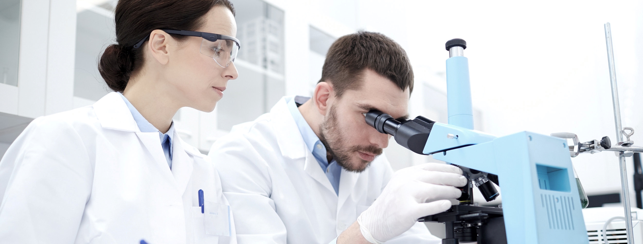 science, chemistry, technology, biology and people concept - young scientists with microscope making test or research in clinical laboratory and taking notes