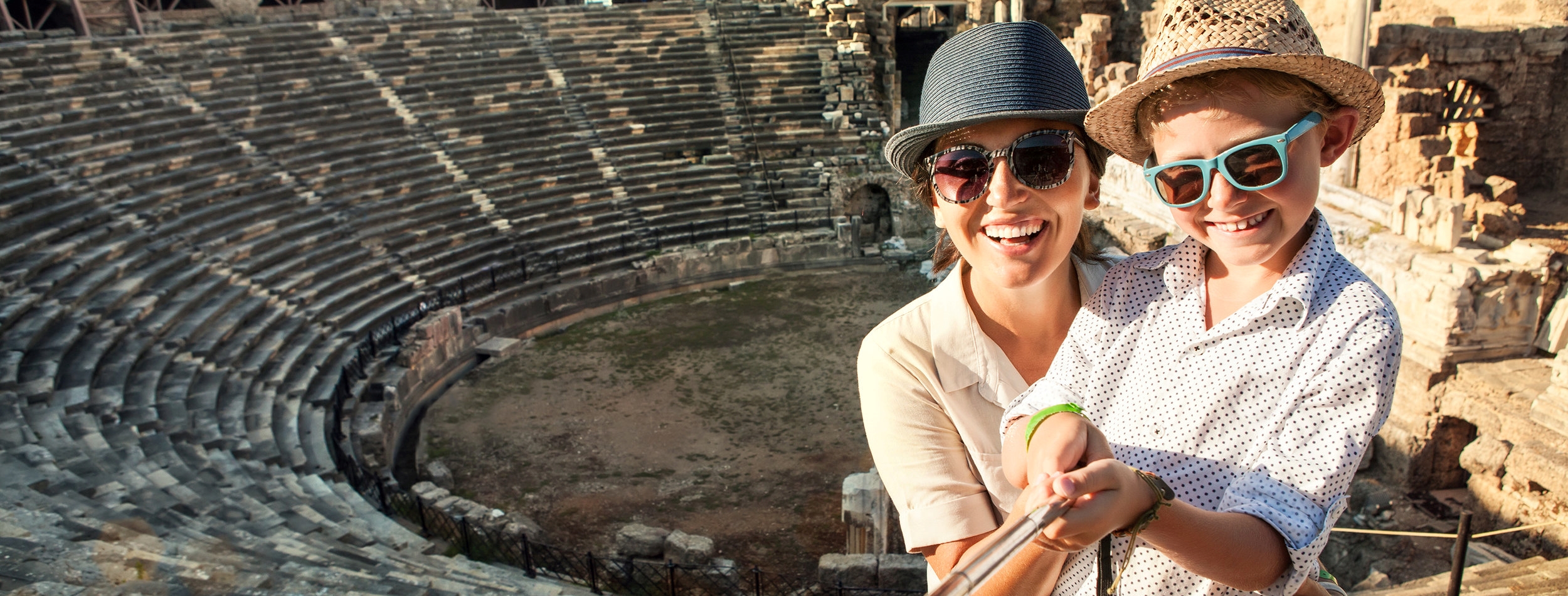 Mother with son smiling to camera taking a selfie photo in antique theatre using a selfie stick. Traveling around the world with kids concept image.