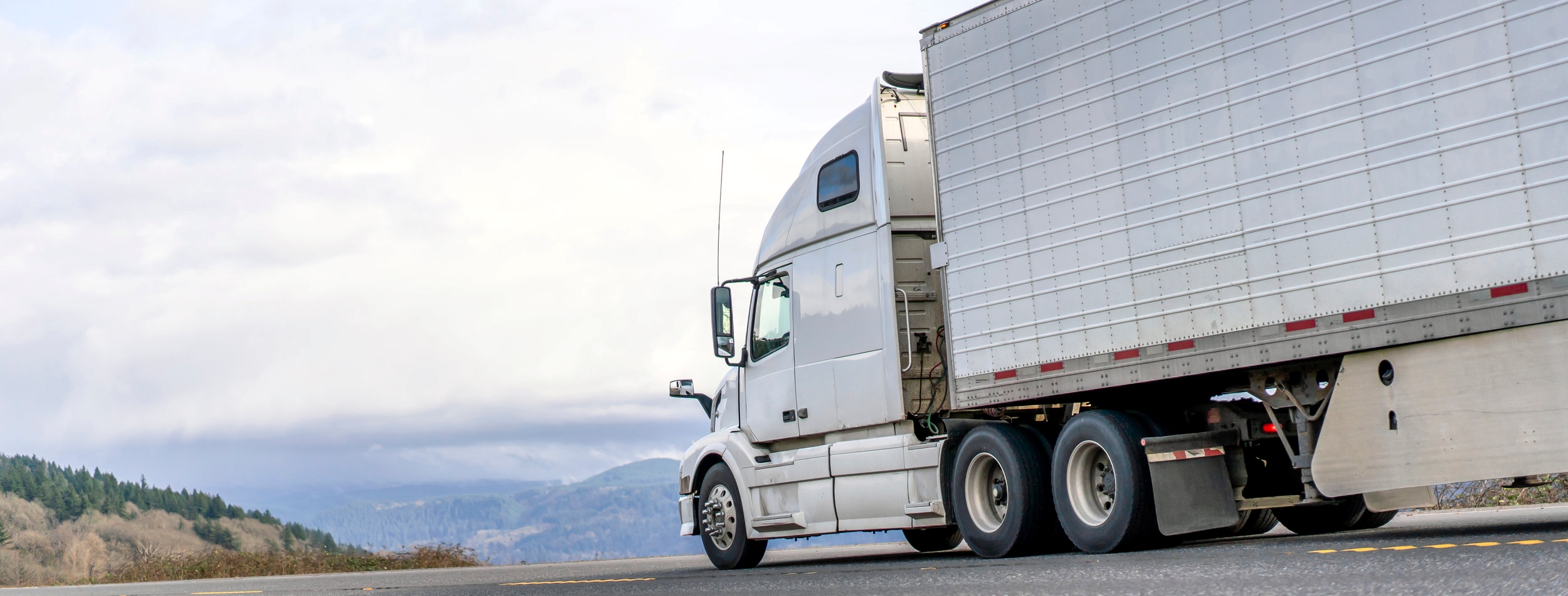 White big rig semi truck transporting food in refrigerator semi trailer driving on the road with sky and hills view