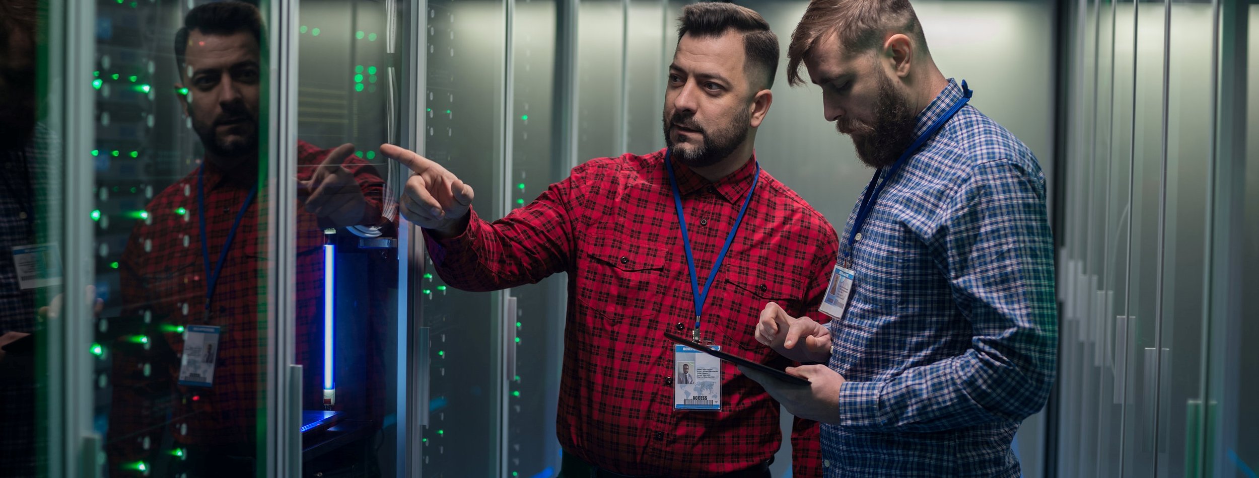 Portrait of two adult bearded man standing in corridor of server room in data center smiling at camera