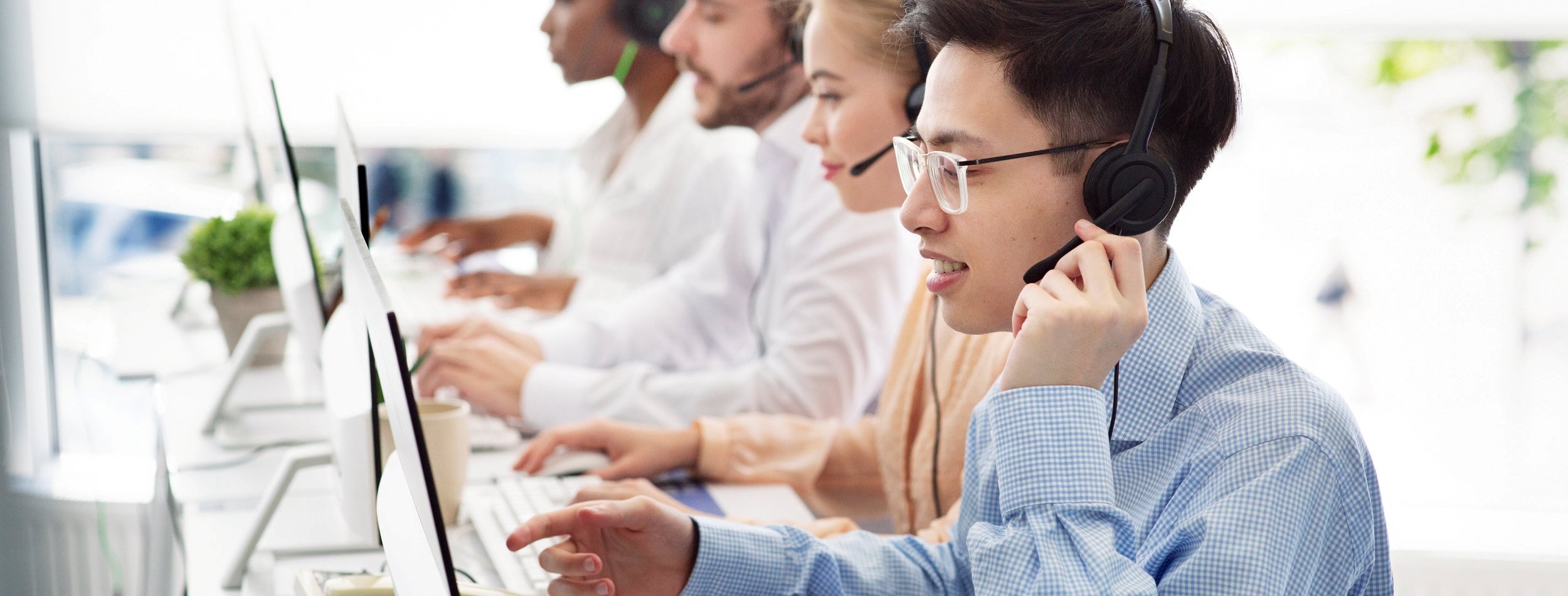 Telecommunications concept. Positive hotline consultants selling goods or services at call centre, copy space. Diverse team of tech support managers dealing with customers needs at modern office