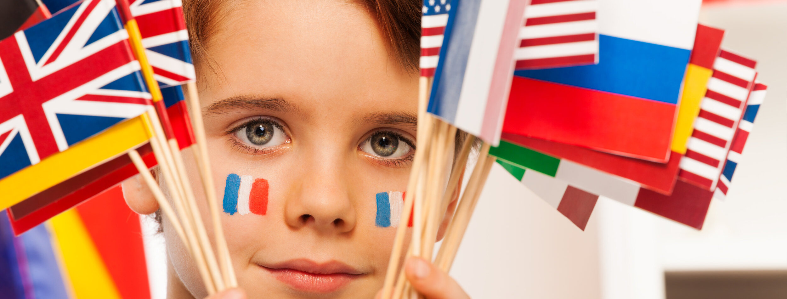 Close up picture of French boy with flags on cheeks hiding behind flags