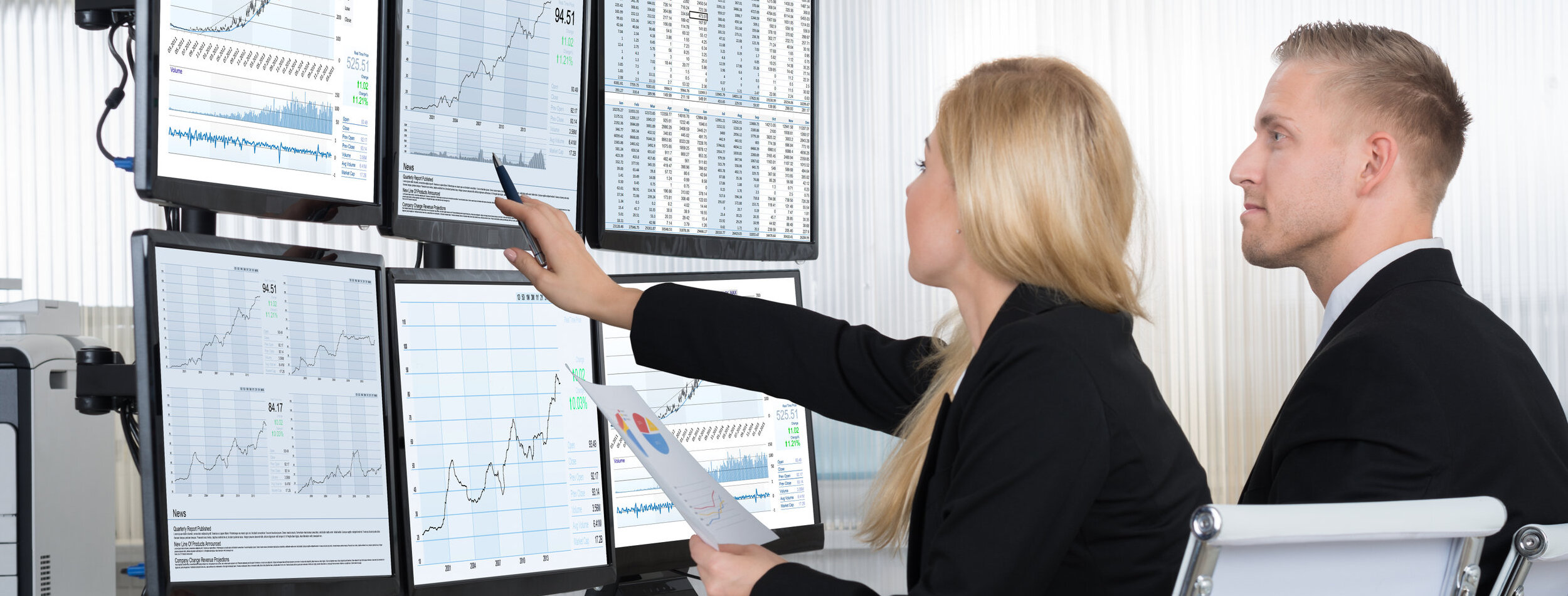 Financial workers analyzing data displayed on computer screens at desk in office