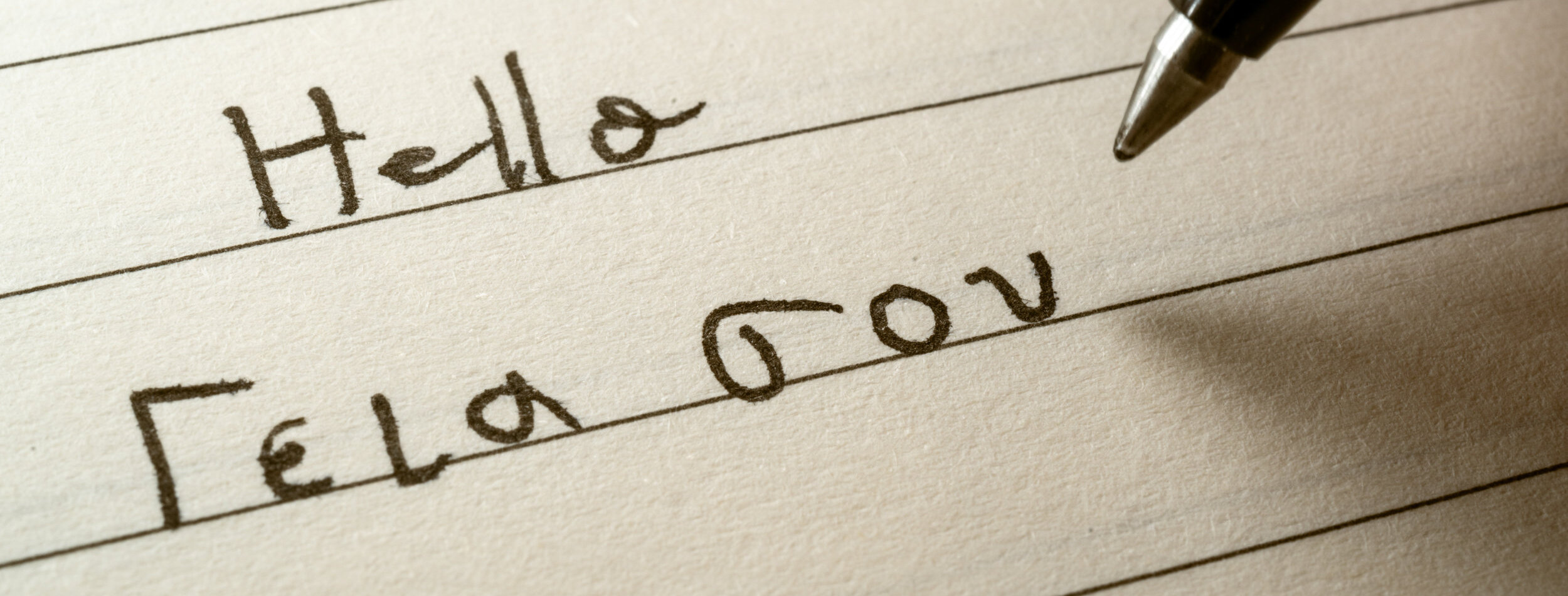 Beginner Greek language learner writing Hello word in greek alphabet on a notebook close-up shot