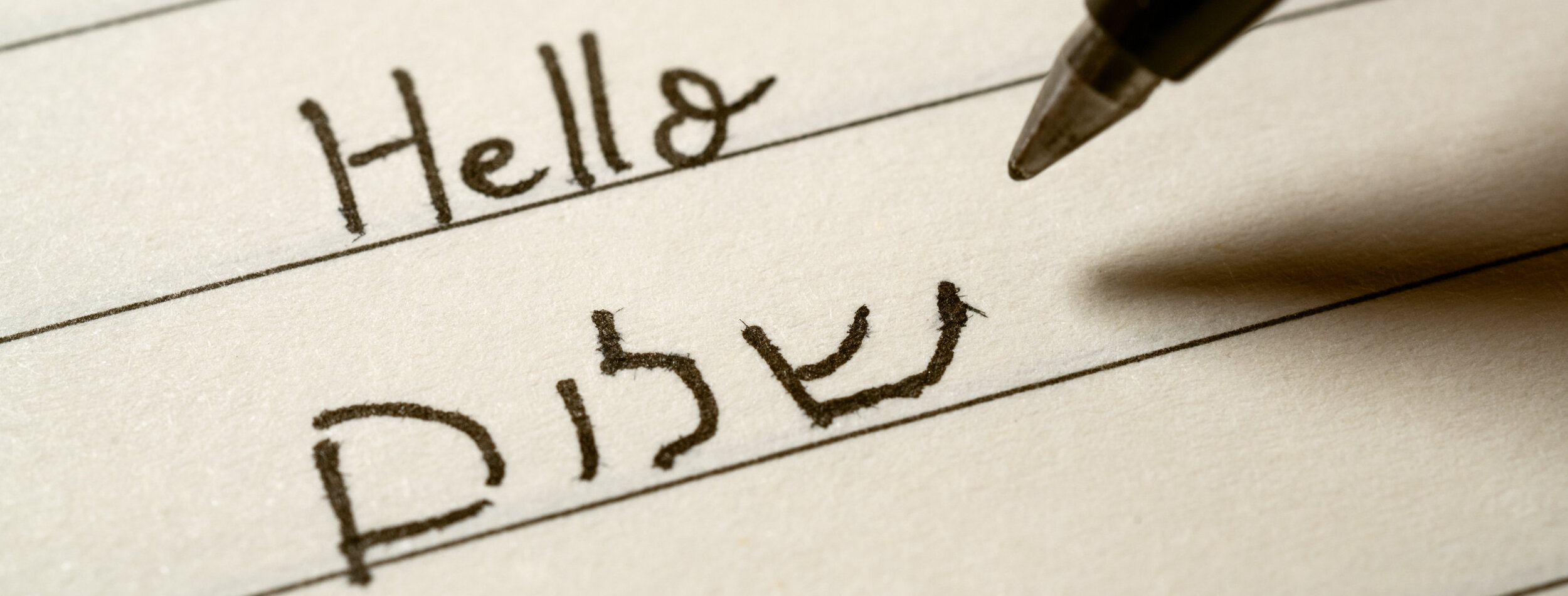 Beginner Hebrew language learner writing Hello shalom word in Hebrew alphabet on a notebook close-up shot