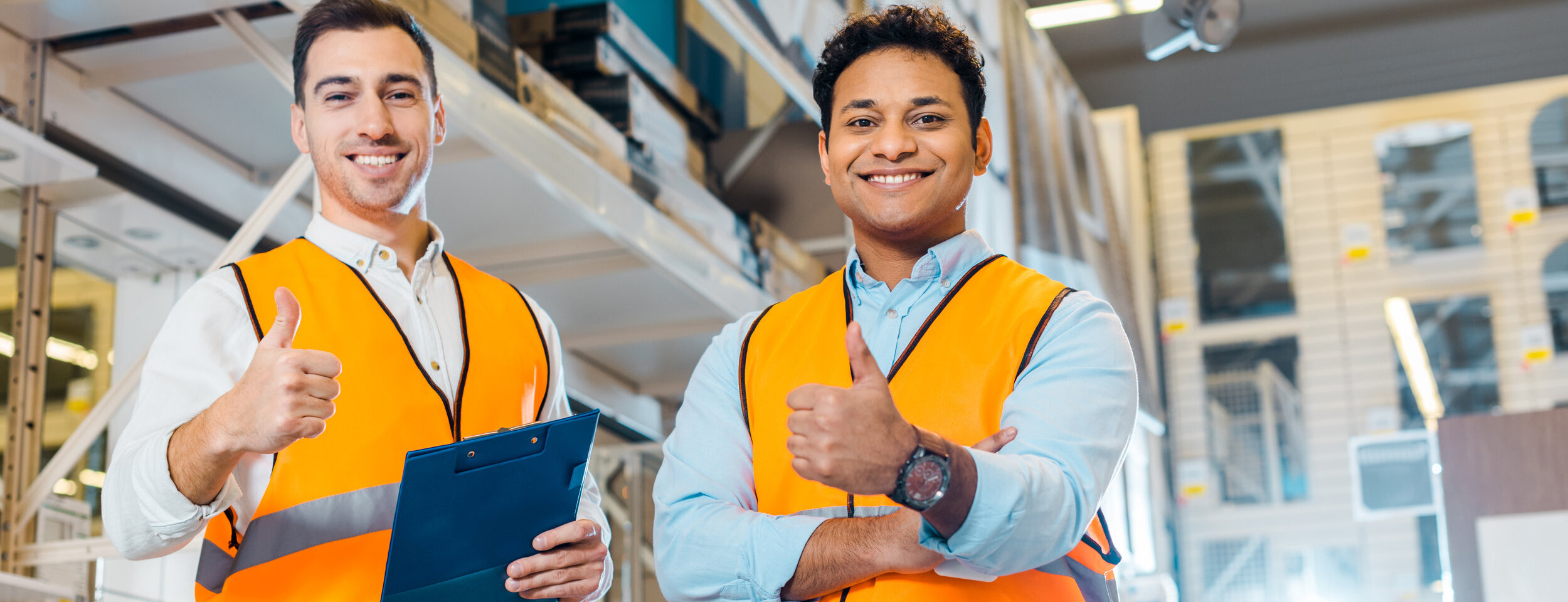 cheerful multicultural warehouse workers showing thumbs up and looking at camera