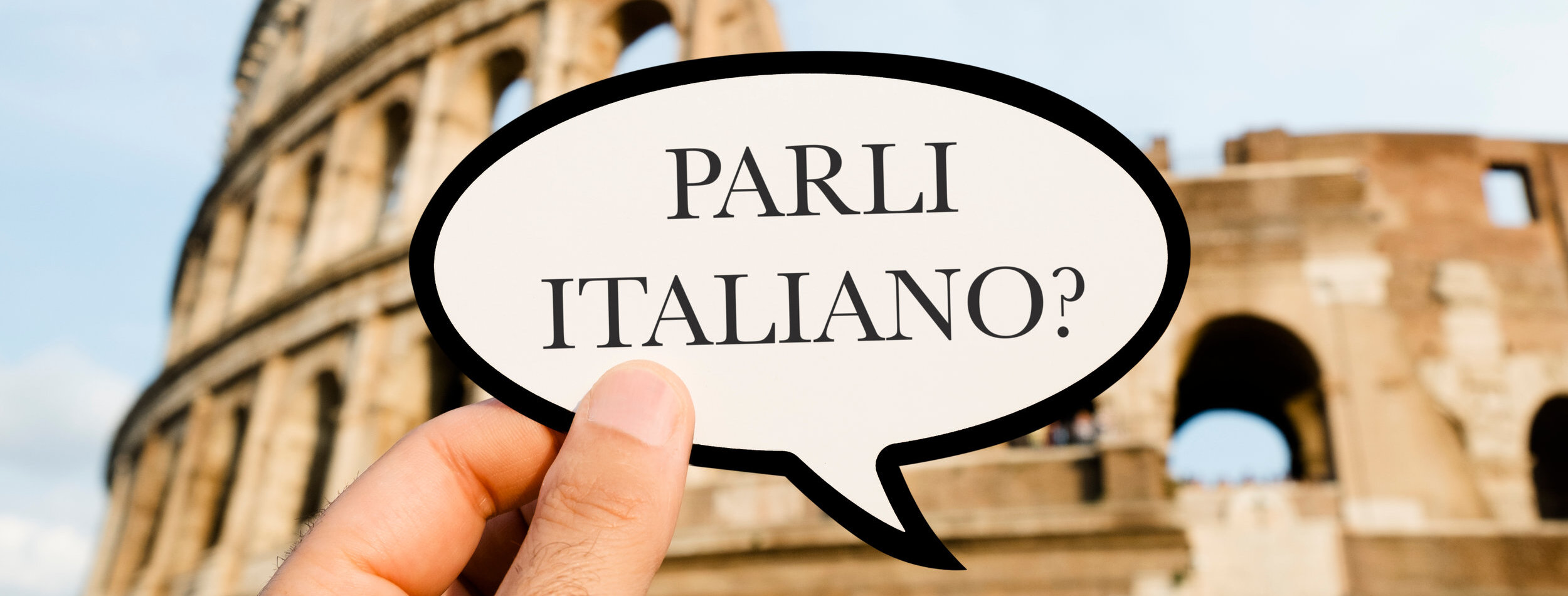 closeup of the hand of a caucasian man holding sign with the question parli italiano? do you speak Italian, written in Italian, in front of the Flavian Amphitheatre or Colosseum, in Rome, Italy