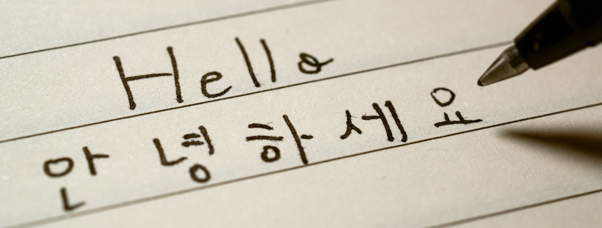 Beginner Korean language learner writing Hello word Annyeonghaseyo in Korean characters on a notebook close-up shot