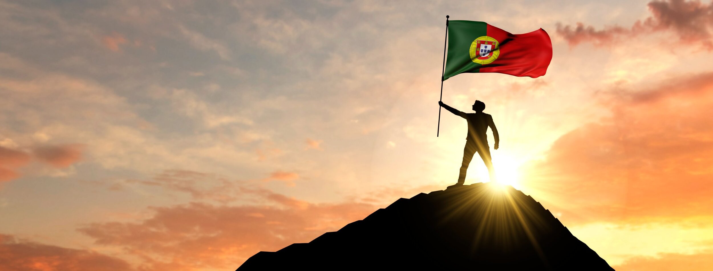 A guy on the top of the mountain showing a portugal flag. 