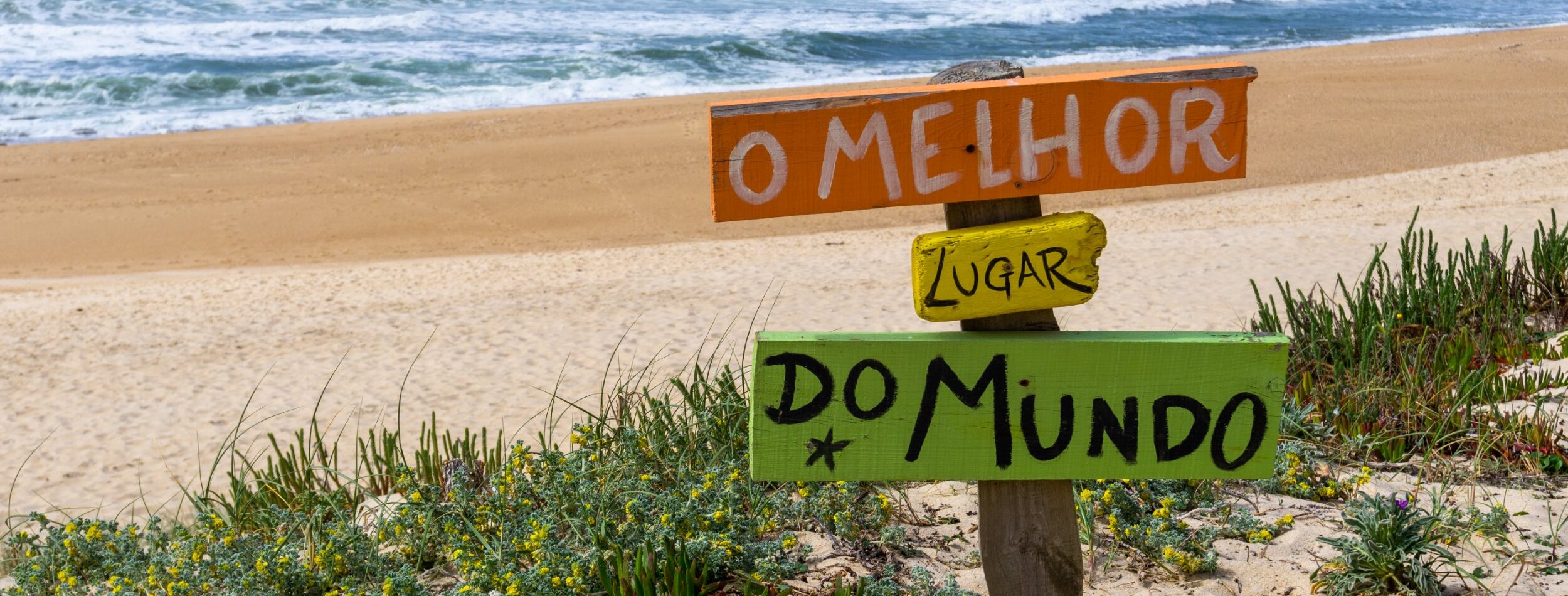 A board on the beach saying "The best place in the world" in portuguese